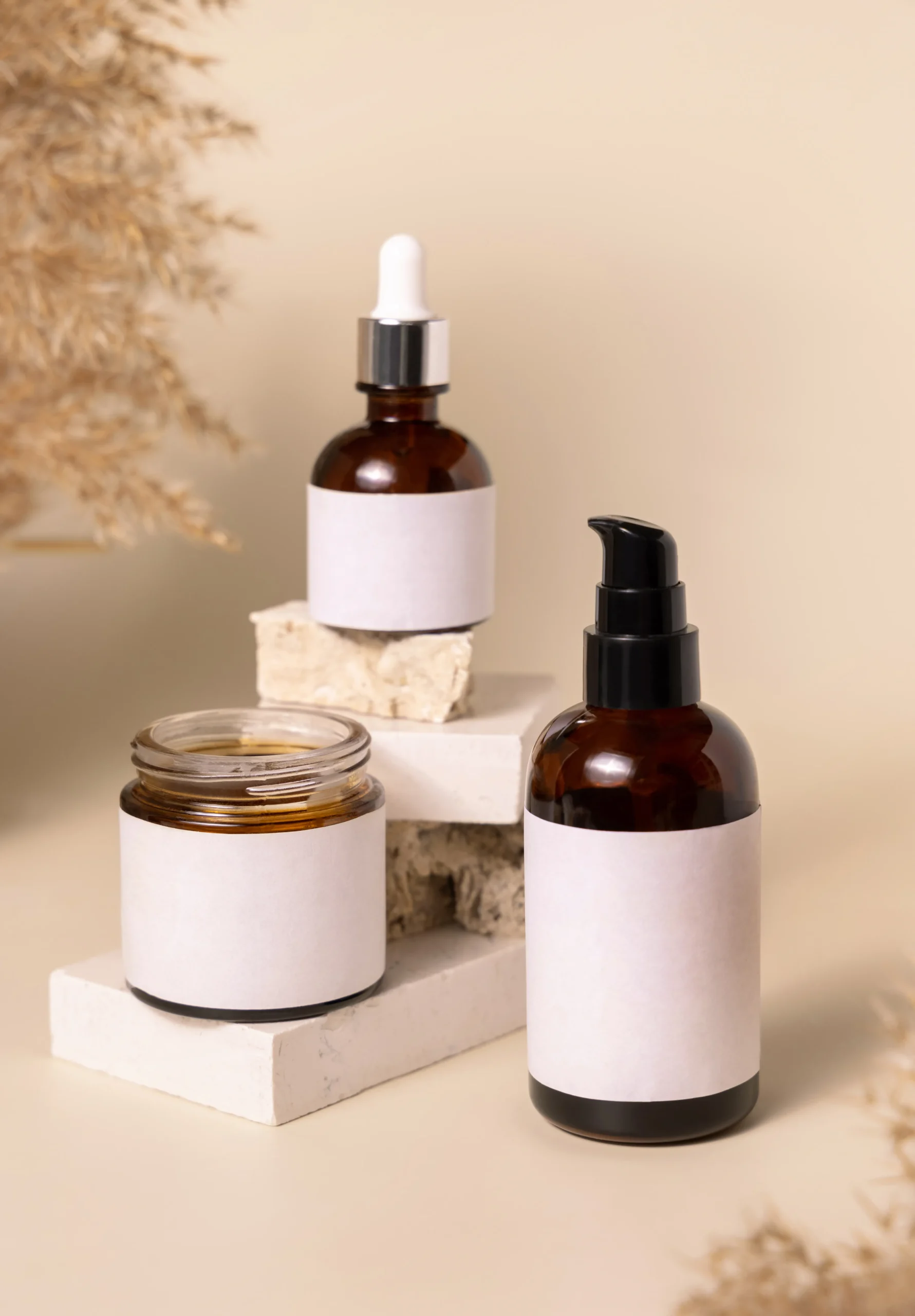 Amber glass cosmetic pump bottle, dropper bottle, and cream jar with blank white labels displayed on stone blocks for private label skincare OEM manufacturing.