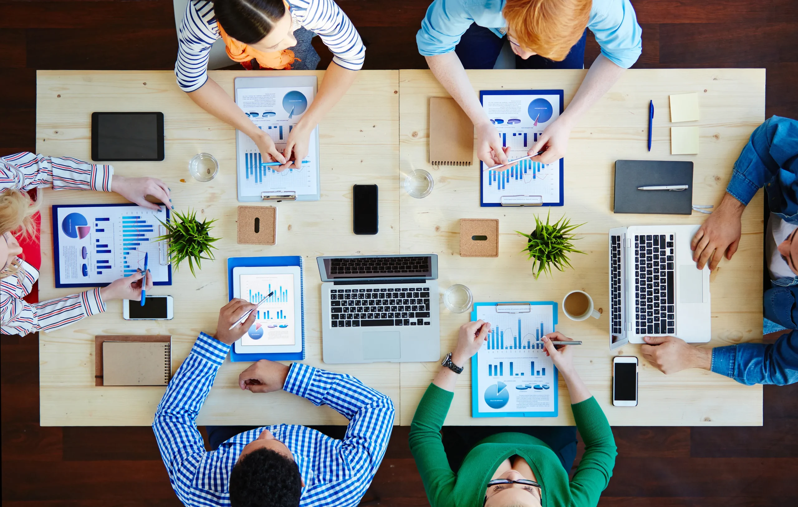 Top-down view of a business marketing team analyzing growth data reports, charts, and digital sales funnels around a wooden conference table for skincare and dietary supplement OEM clients.