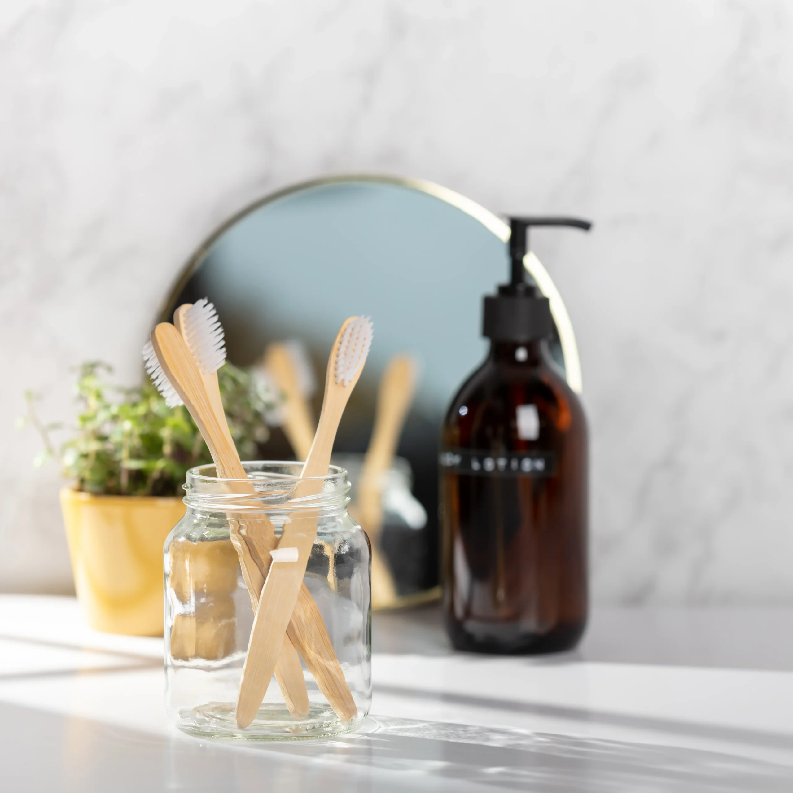 Amber glass lotion dispenser bottle paired with bamboo toothbrushes in a glass jar on a bright bathroom vanity for natural personal care OEM services.