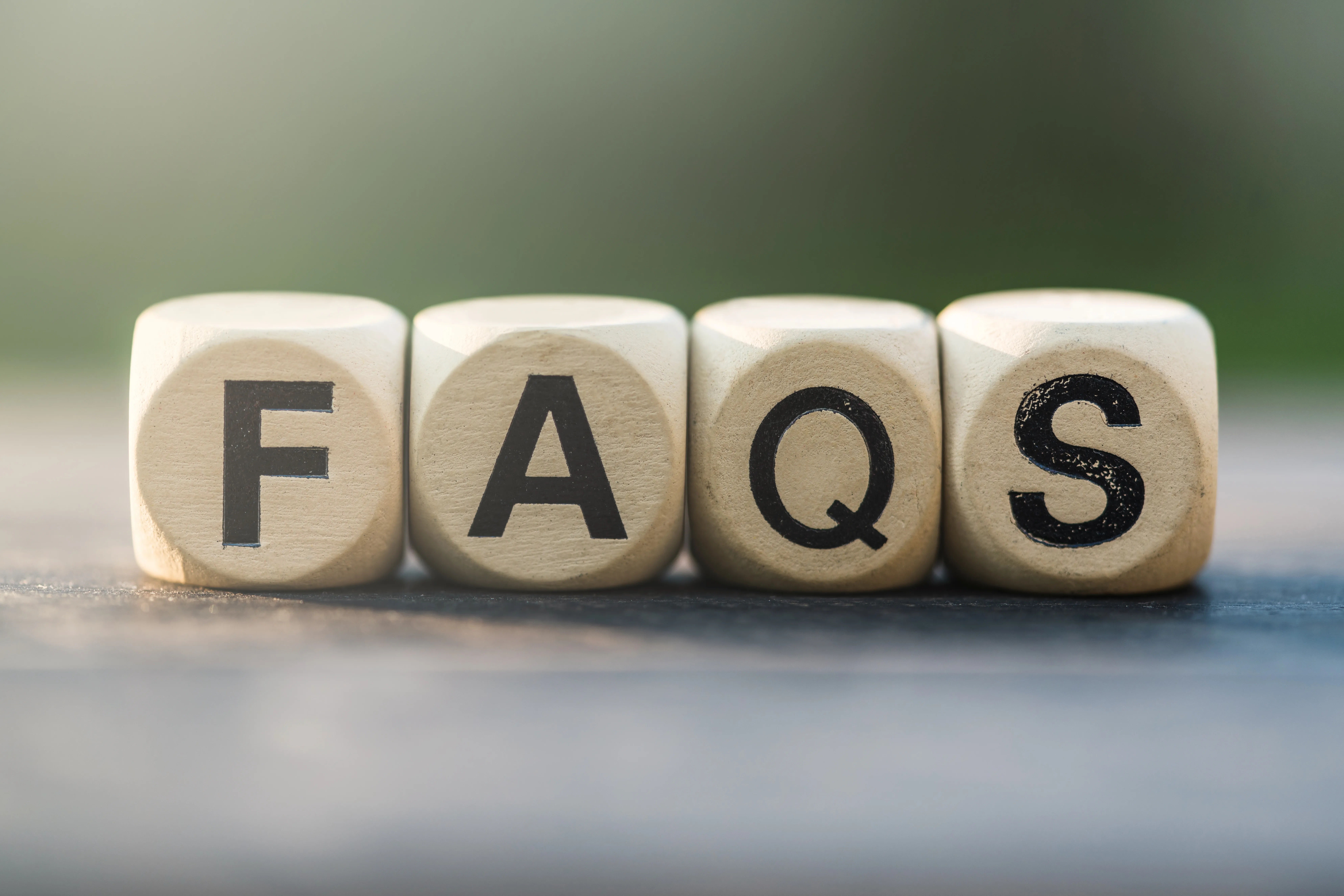 Wooden dice blocks spelling the word FAQs in black letters lined up on a wooden table for frequently asked questions about skincare and dietary supplement OEM ODM manufacturing services.