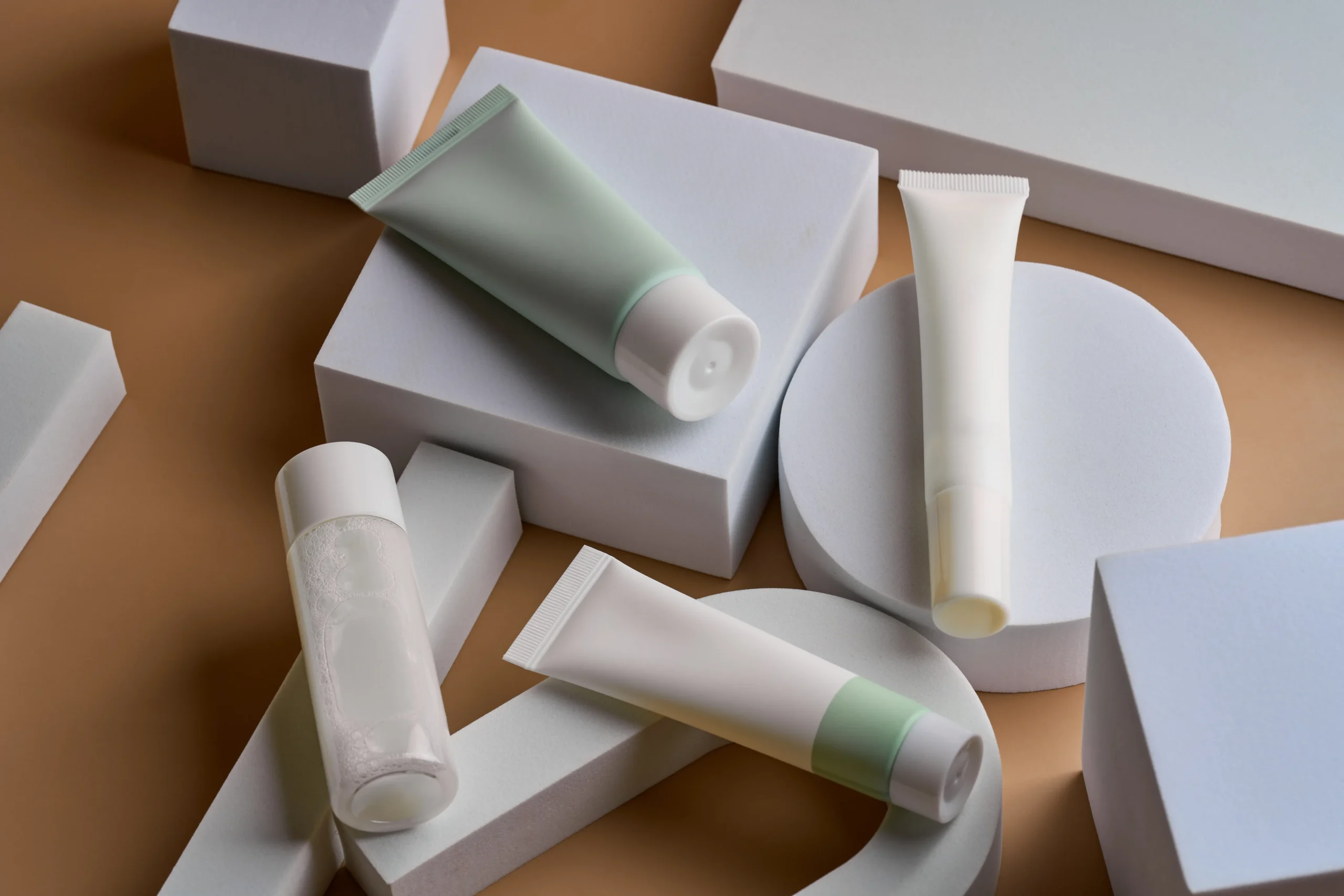 บรรจุภัณฑ์และการออกแบบ Assorted cosmetic squeeze tubes and toner bottle arranged on white geometric display blocks for private label cosmetic packaging design.