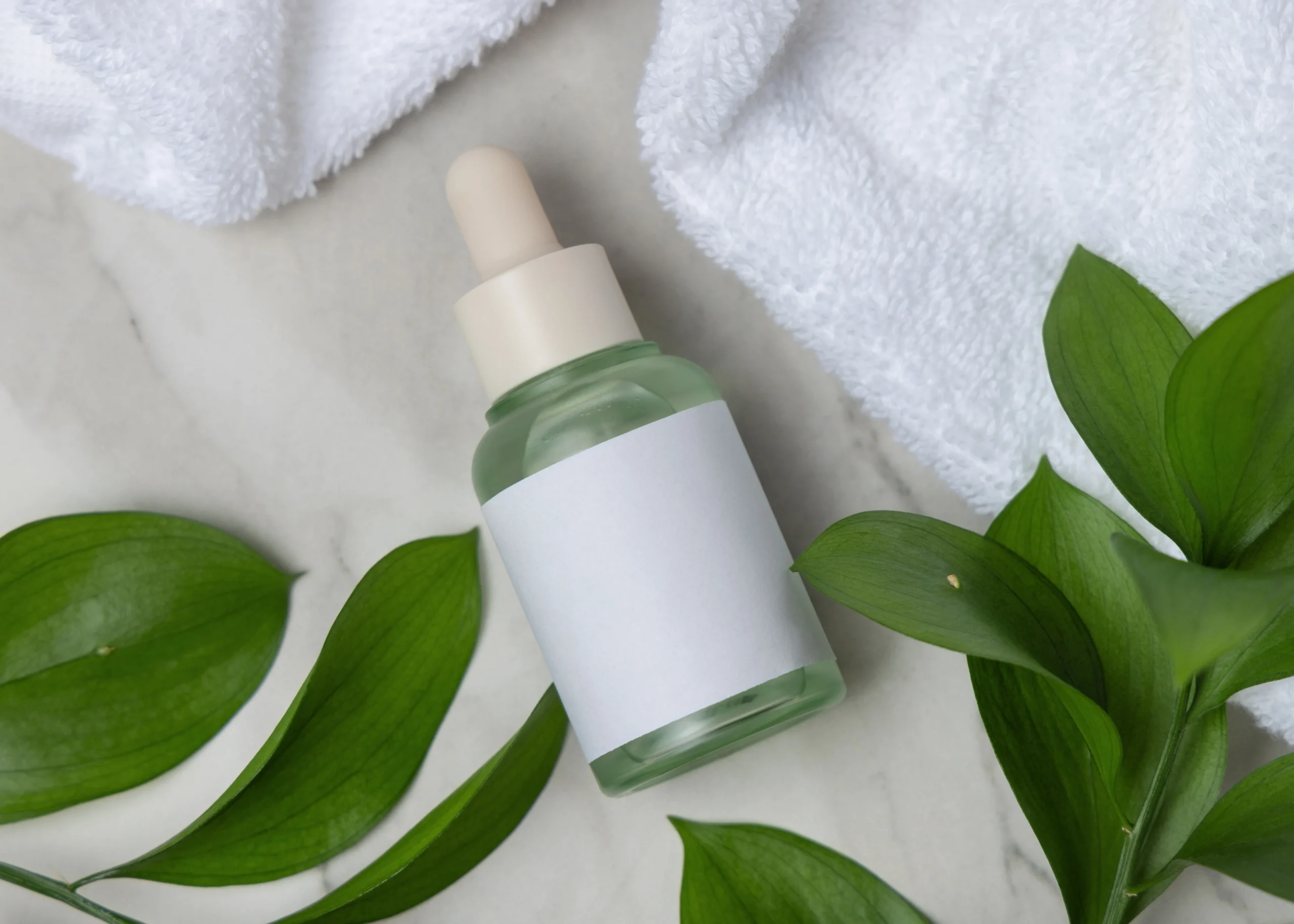 OBM TH Frosted green serum dropper bottle featuring a blank label lying beside fresh botanical leaves and a white fluffy spa towel on marble stone.